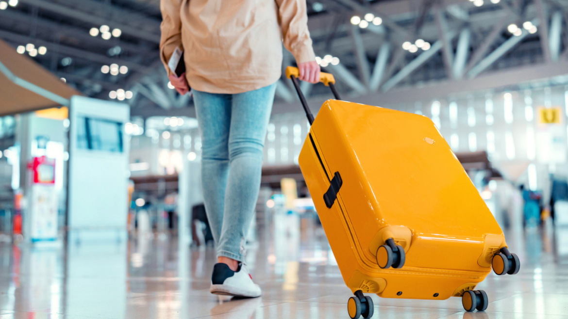 Close up shot of young woman carrying yellow suitcase through airport.